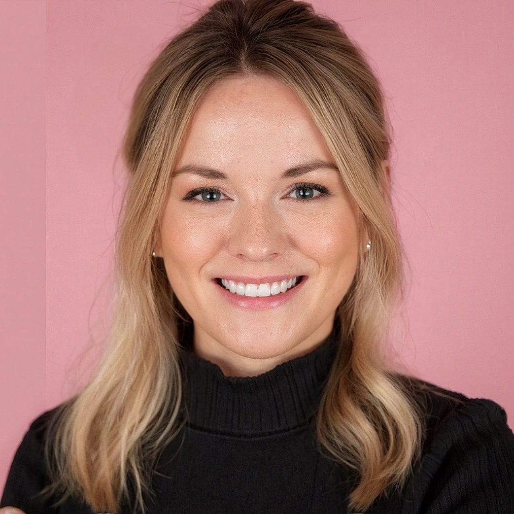 Smiling woman in black sweater on pink background.