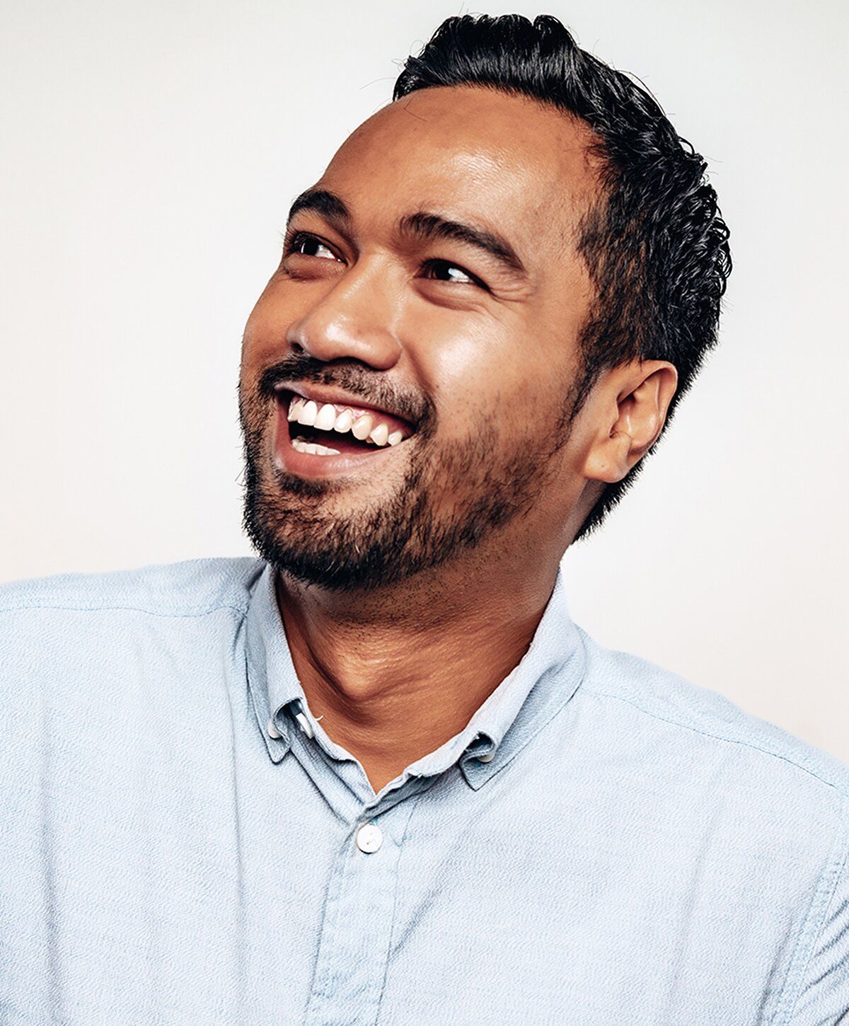 Smiling man in denim shirt against neutral background.