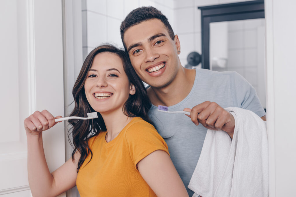 happy multiracial couple holding toothbrushes in bathroom